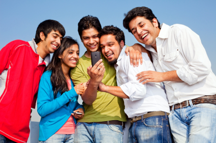 Five Young Cheerful Indian Friends reading and sharing SMS Joke on a cell phone